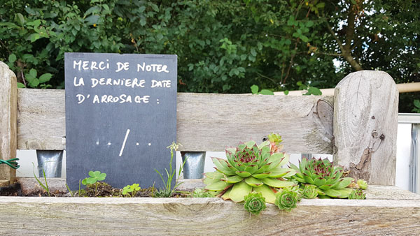 Pancarte en ardoise-date d'arrosage du jardin partagé sur le récupérateur d'eau de pluie